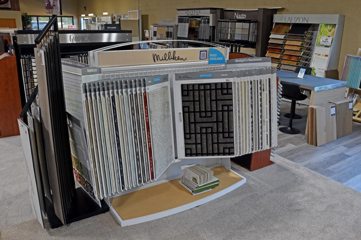 A display of carpet and flooring samples in a showroom, featuring various textures and patterns, with sample boards and a swatch display rack.